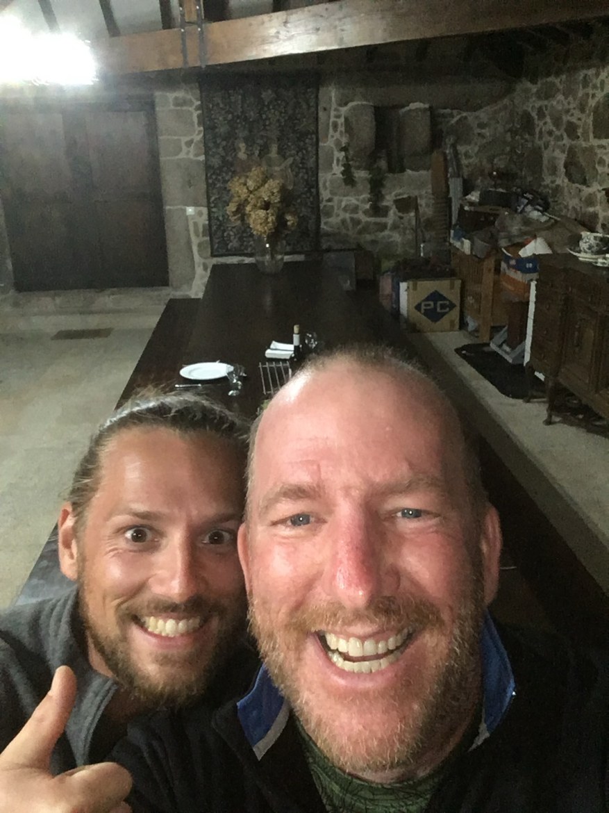 Two pilgrims grinning in a stone-walled dining room