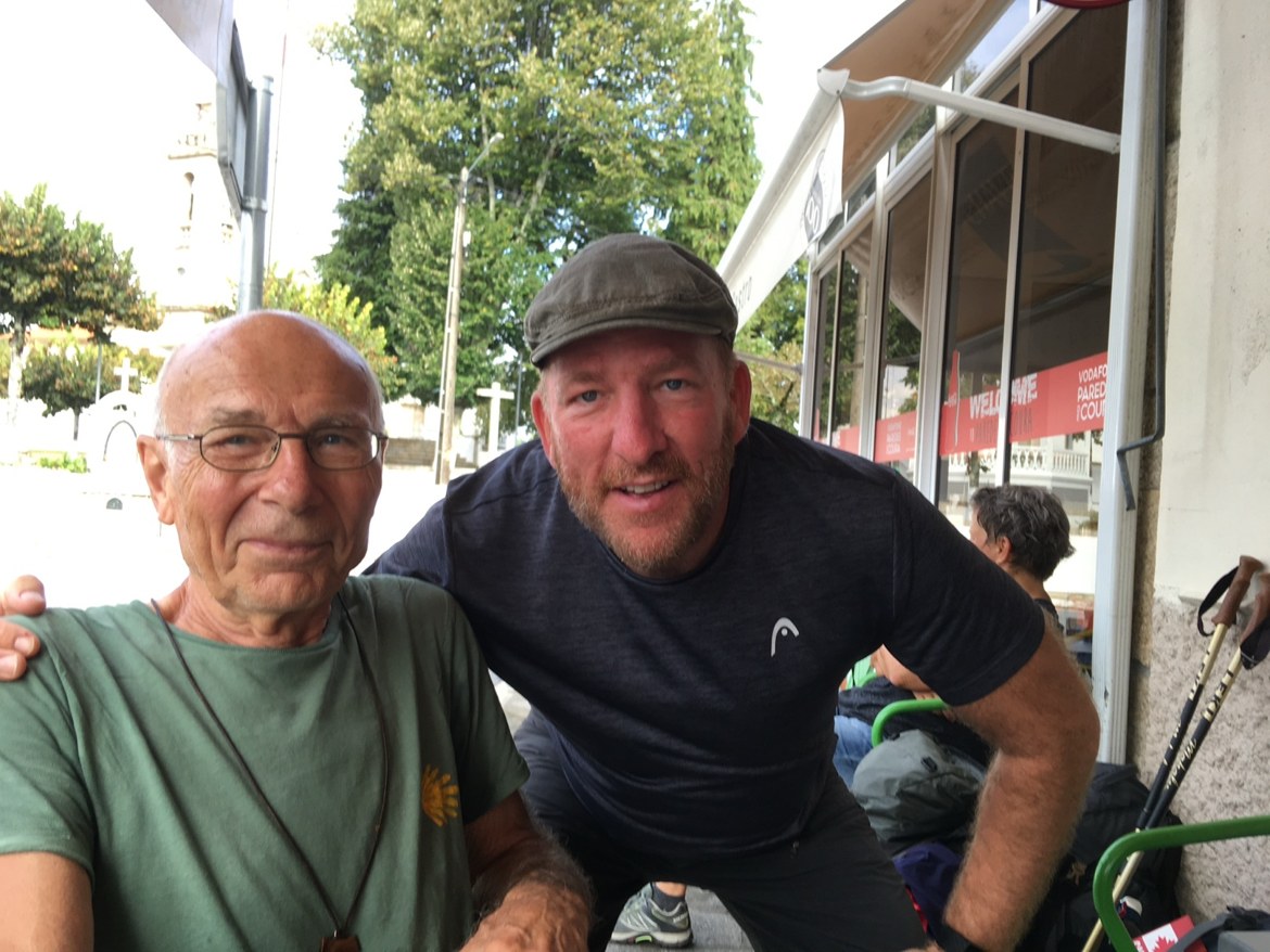 A pilgrim posing with an older fellow pilgrim outside a café