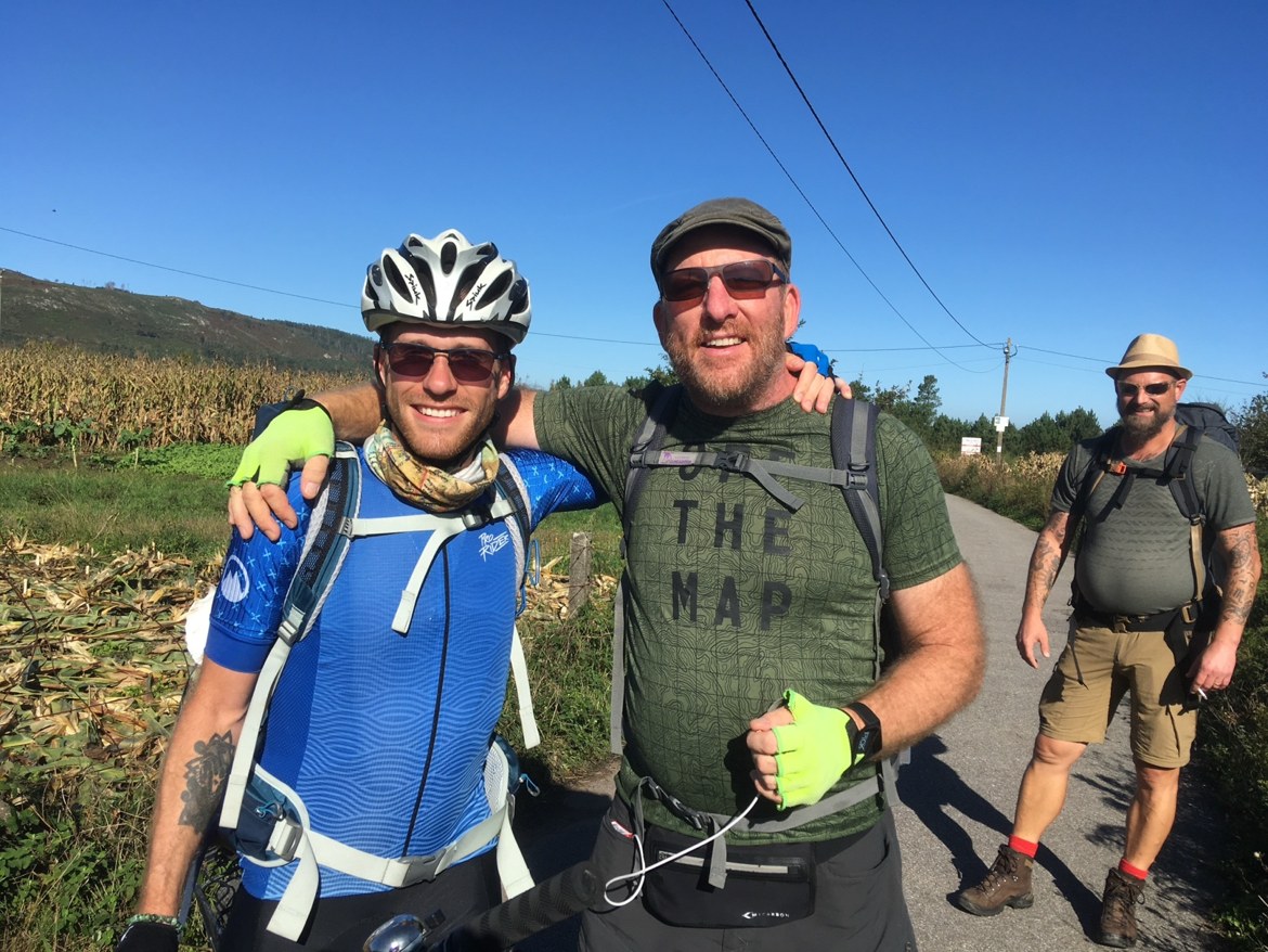 Two pilgrims posing with a cyclist on a country road