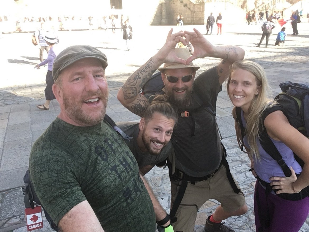 Four pilgrims in the cathedral square in Santiago, one making a heart with his hands