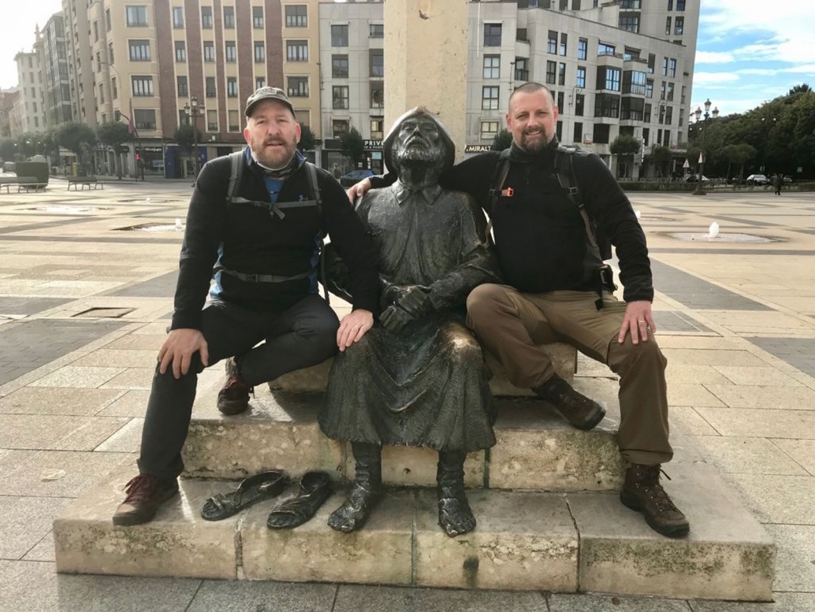 Two pilgrims posing with a bronze statue of a seated pilgrim