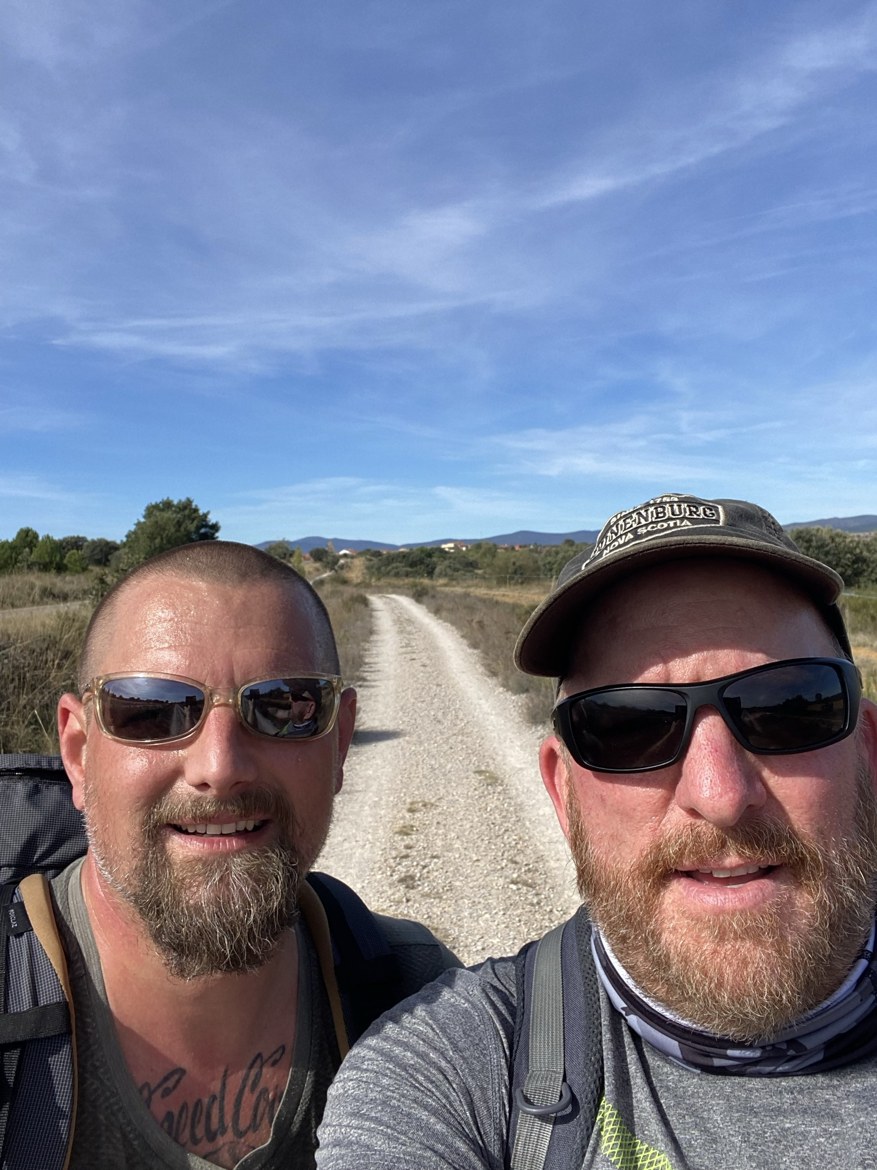 Two pilgrims taking a selfie on a long straight gravel trail across the plain