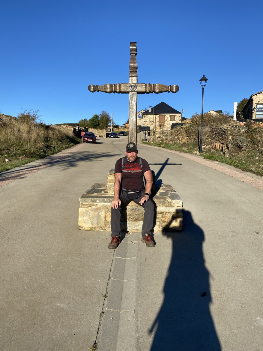 A pilgrim sitting beneath a tall wooden cross