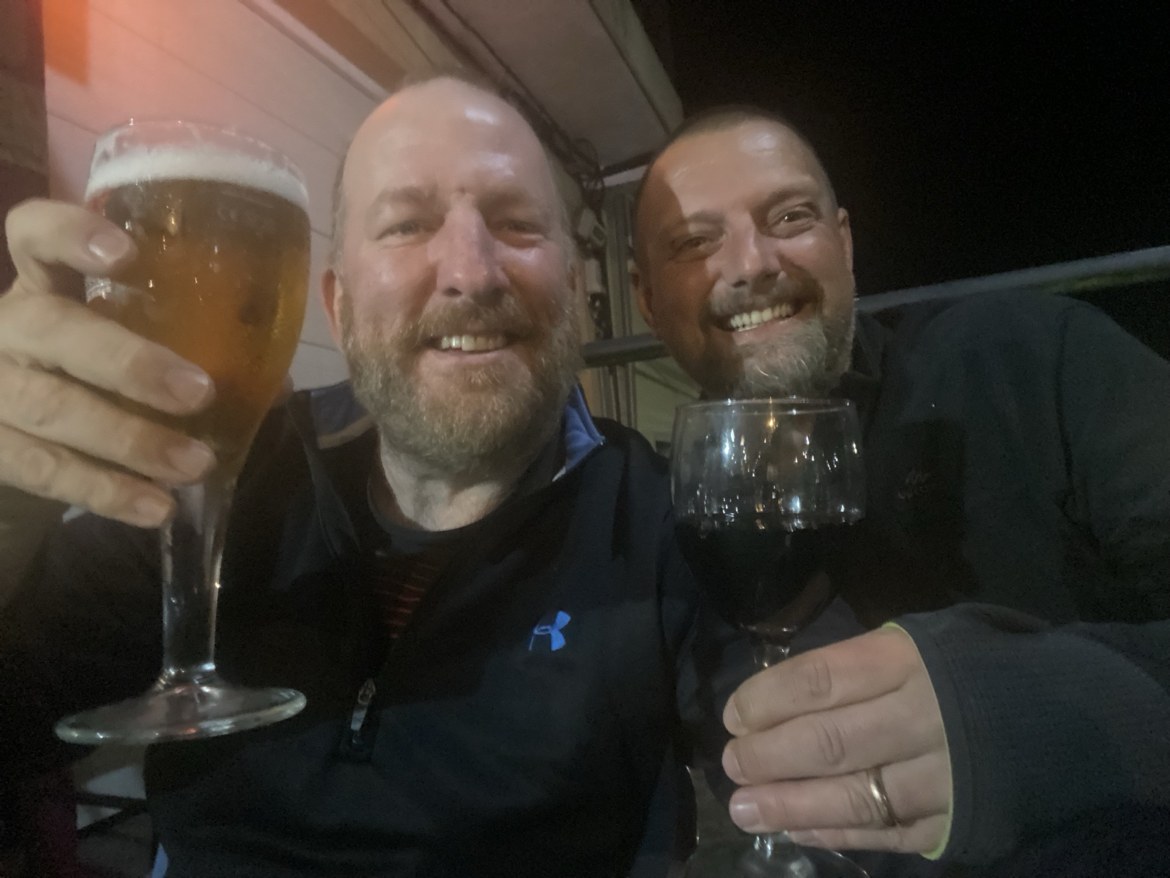 Two pilgrims raising a beer and a wine glass at night