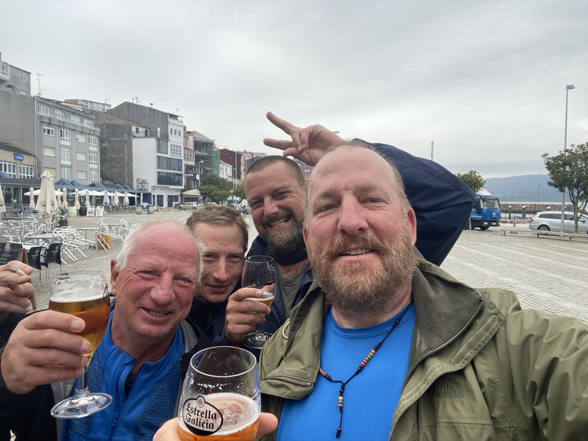 Four pilgrims raising glasses of Estrella Galicia in a seaside town