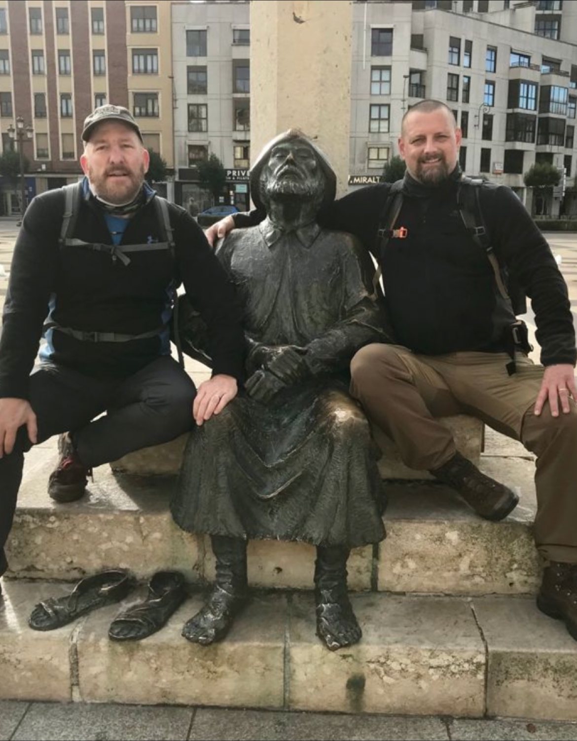 Mike and Nicki posing with a bronze statue of a seated pilgrim in a Spanish city square