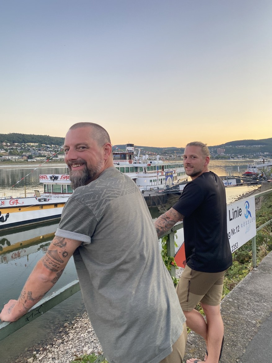 Nicki and Dennis at a Rhine landing at dusk, with a paddle steamer on the river behind them