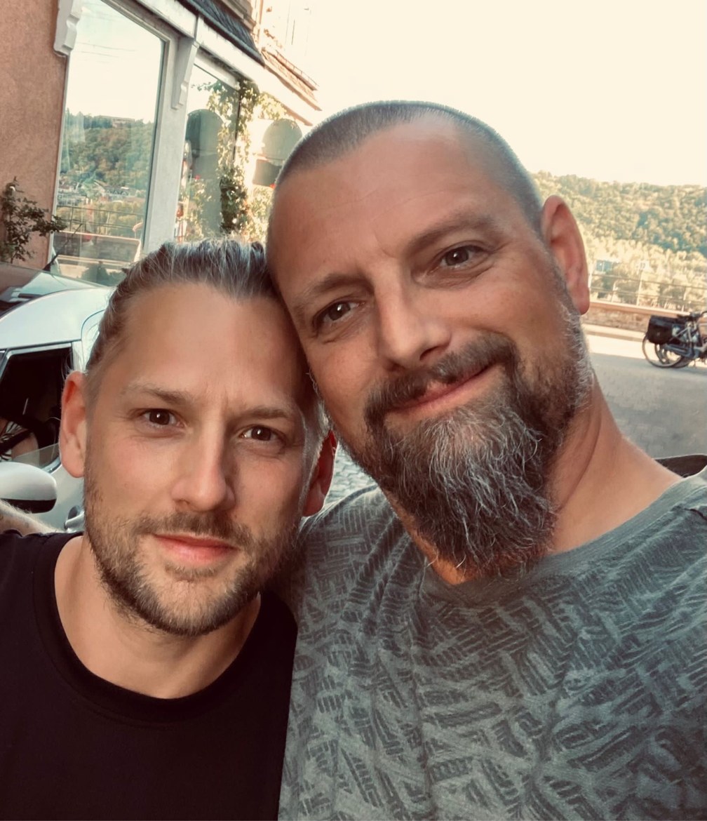 Dennis and Nicki in a close selfie by a riverfront building