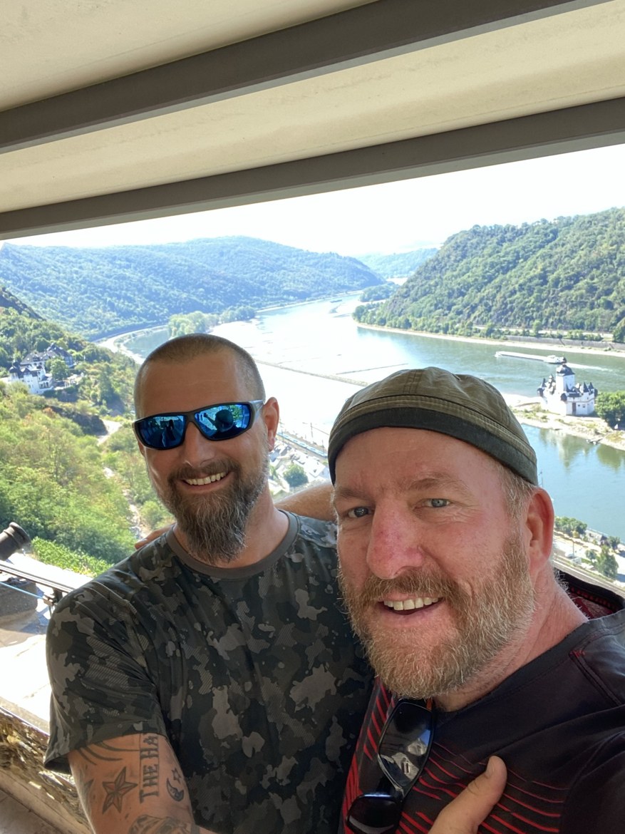 Nicki and Mike taking a selfie above a bend in the Rhine with Pfalzgrafenstein castle on its island below