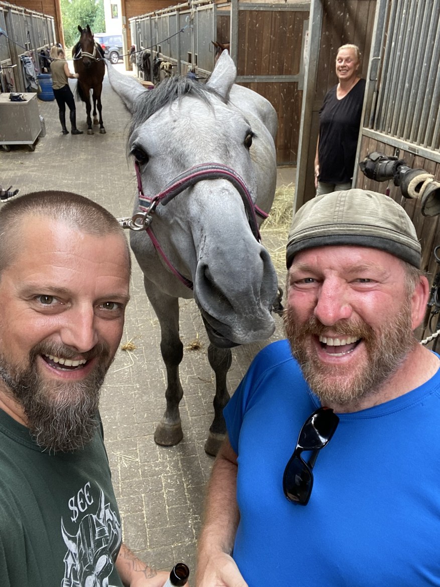 A grey horse putting its nose into a selfie with Nicki and Mike at a stable