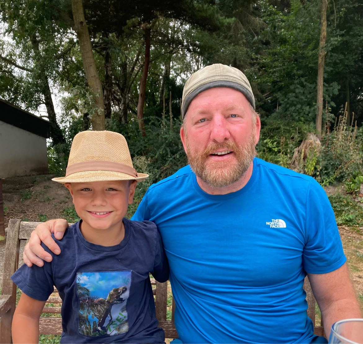 Mike with his arm around a young boy, both wearing straw hats