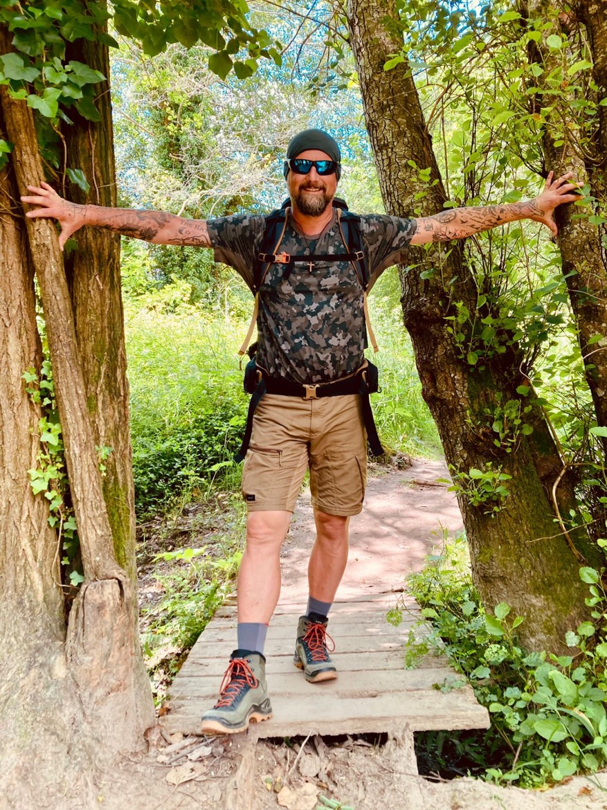 Nicki on a wooden footbridge holding onto two trees, arms spread