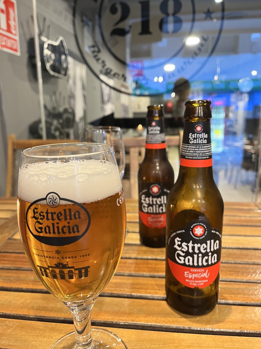 A glass and two bottles of Estrella Galicia on a bar table