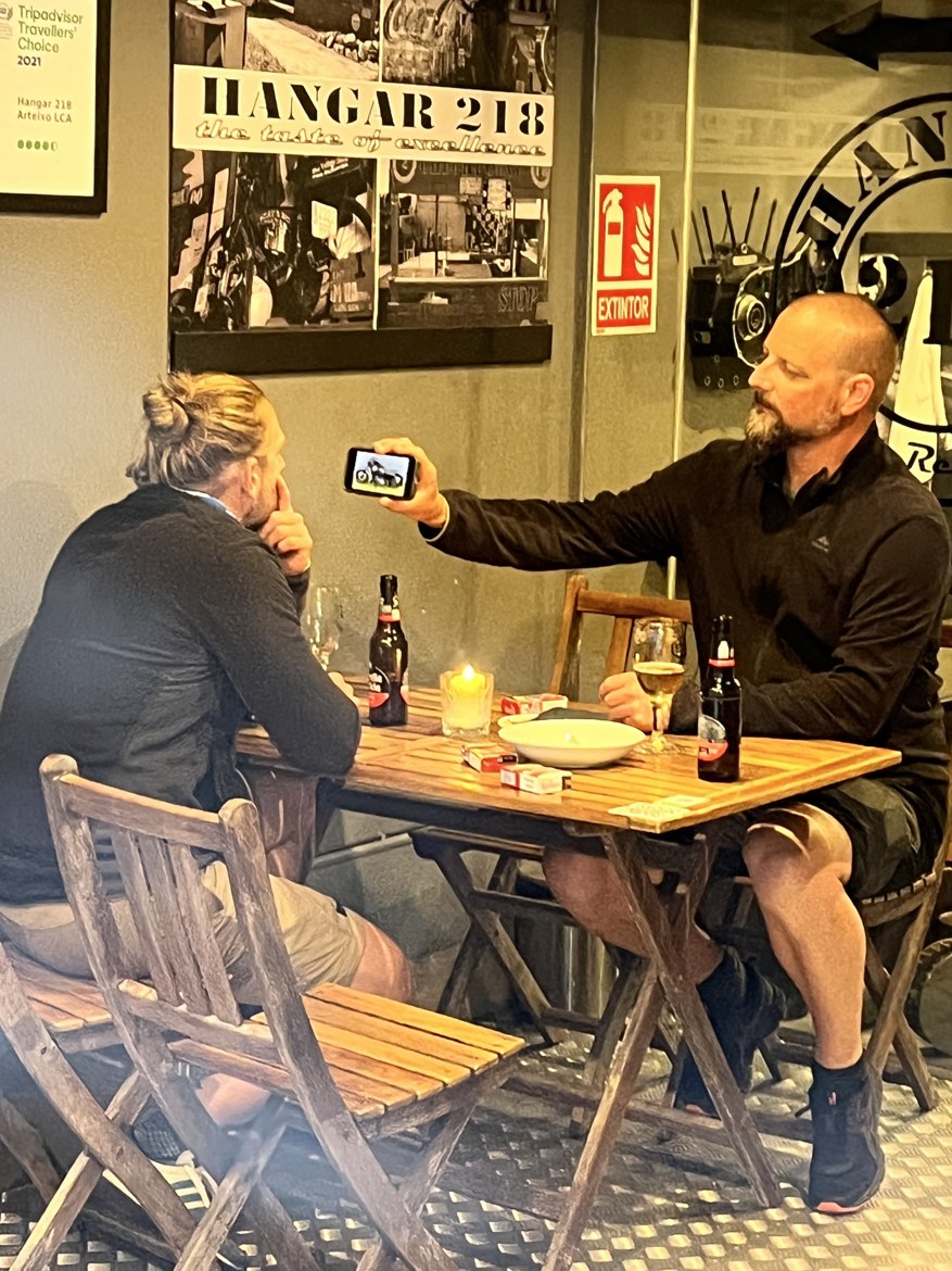 Nicki showing Dennis a photo on his phone across a bar table at Hangar 218