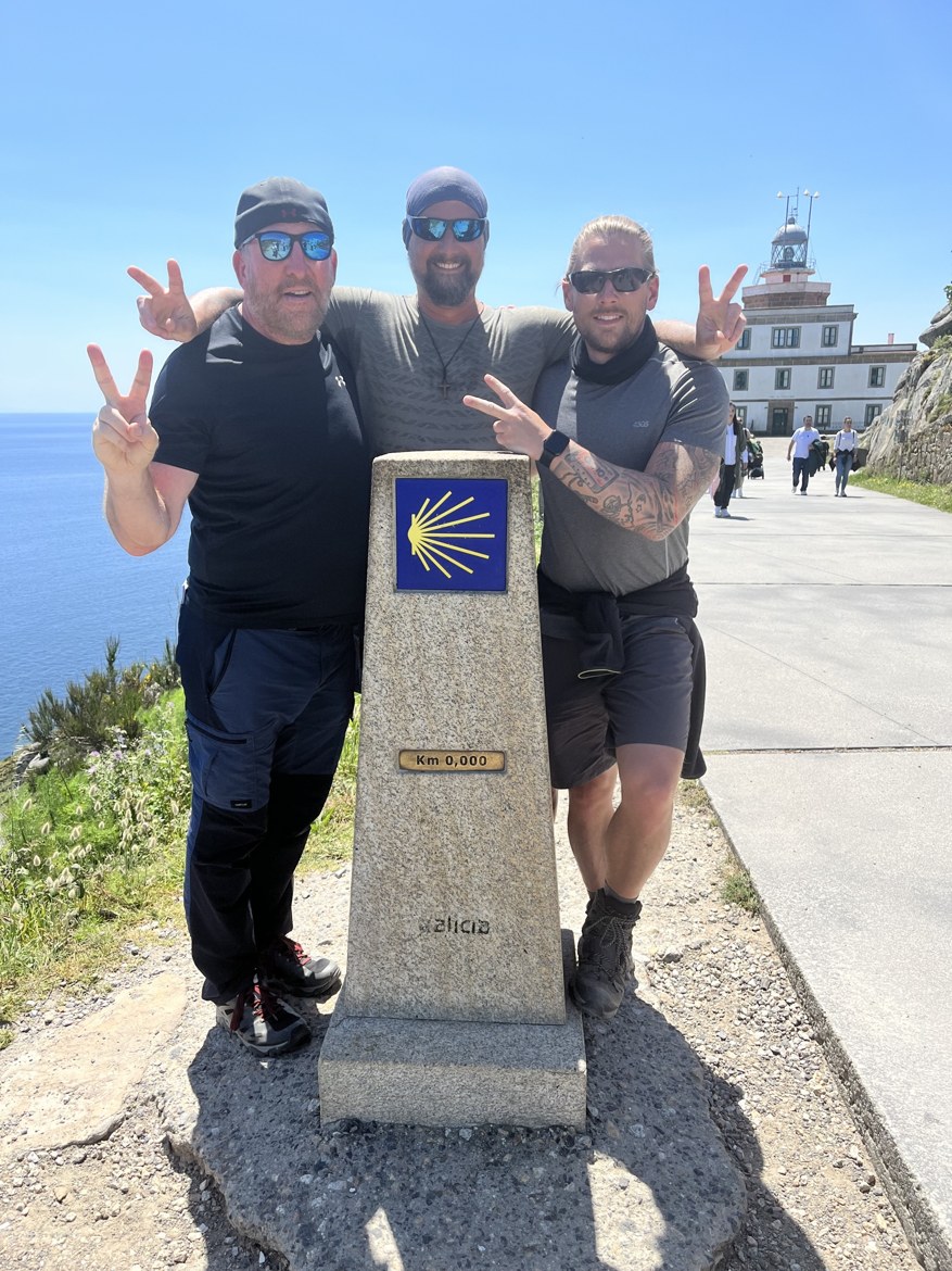 The three brothers around the Km 0,000 marker at Finisterre, the lighthouse behind them
