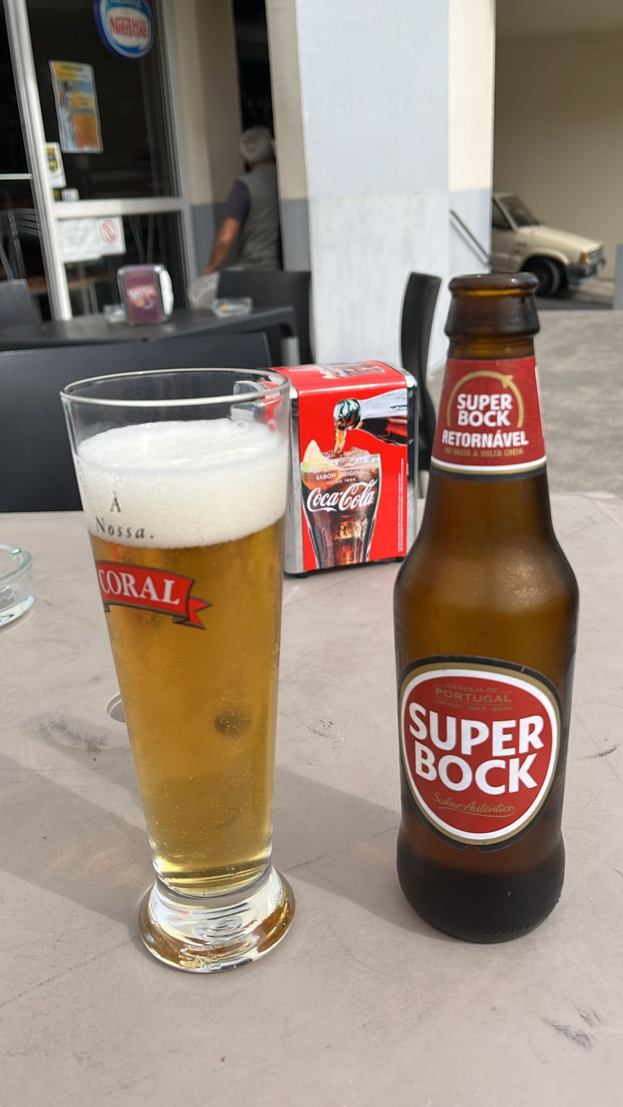 A bottle of Super Bock beer beside a full glass on a cafe table