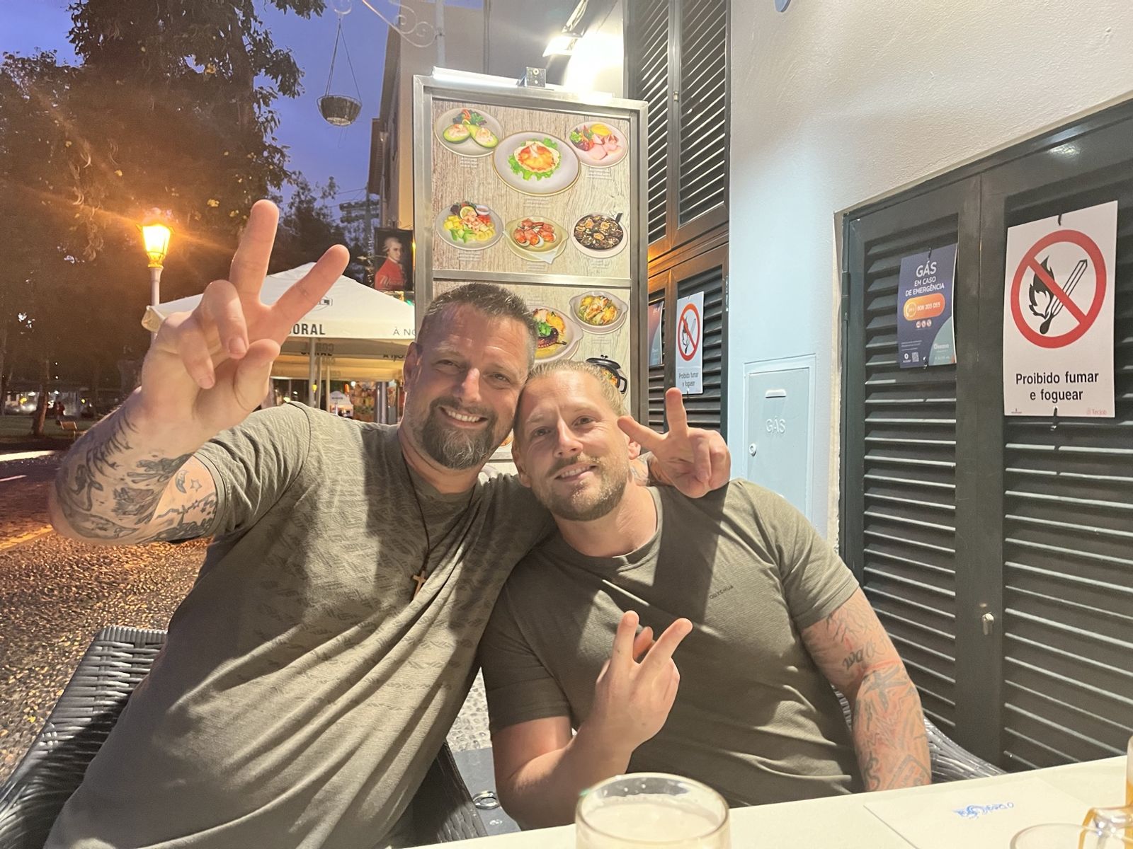 Nicki and Dennis at an outdoor restaurant table in Funchal at dusk, making peace signs