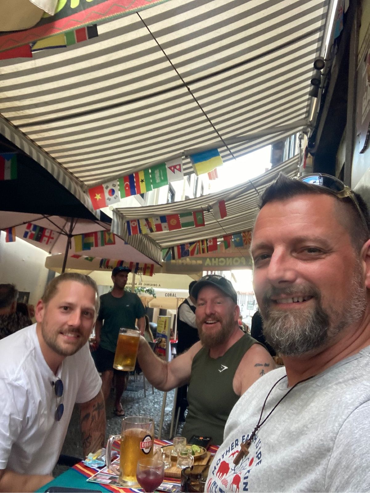 The three Camino Brothers at a bar strung with world flags, raising beers