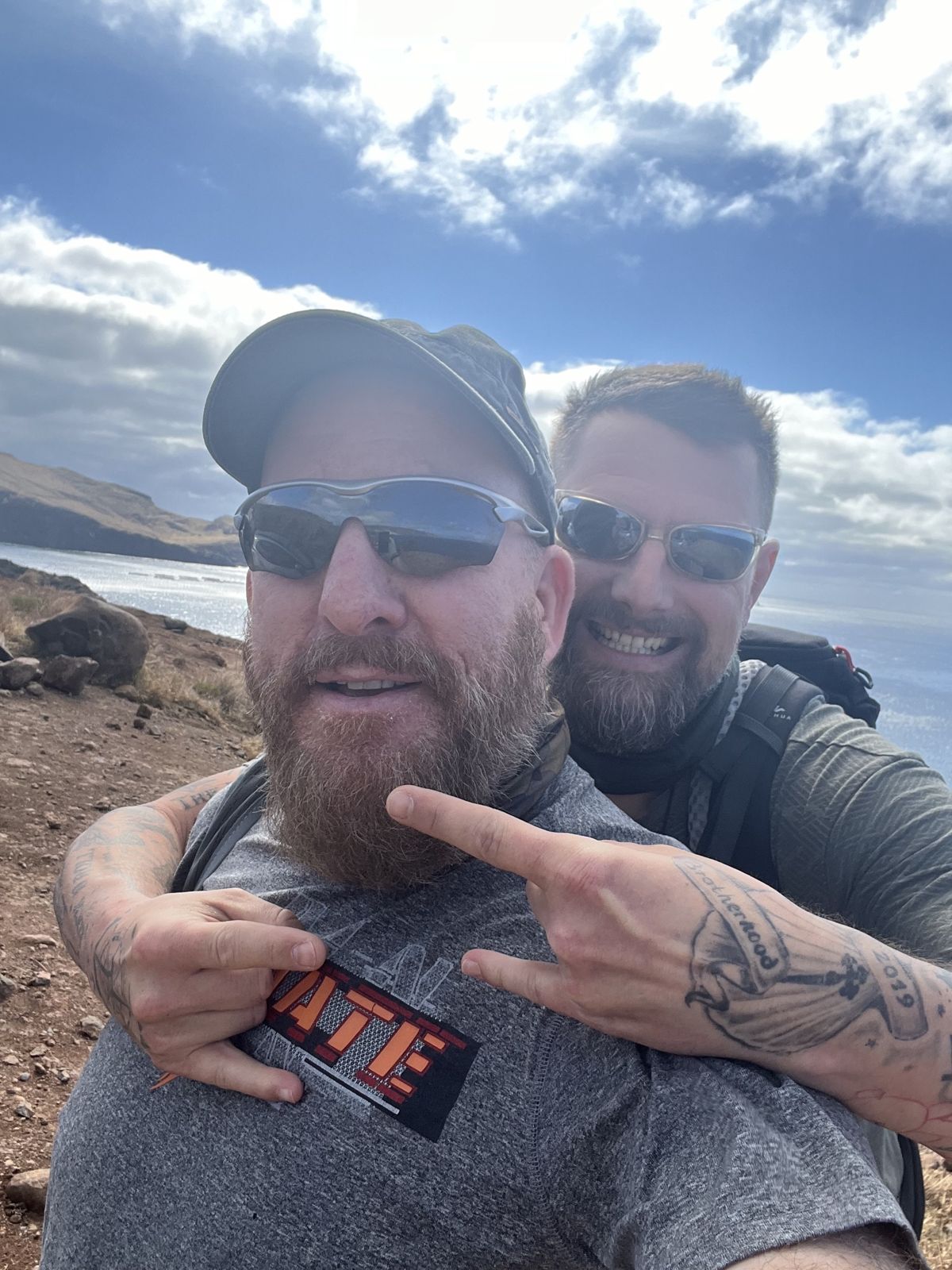 Mike and one of the brothers taking a selfie on the coast, the brother's Brotherhood tattoo visible
