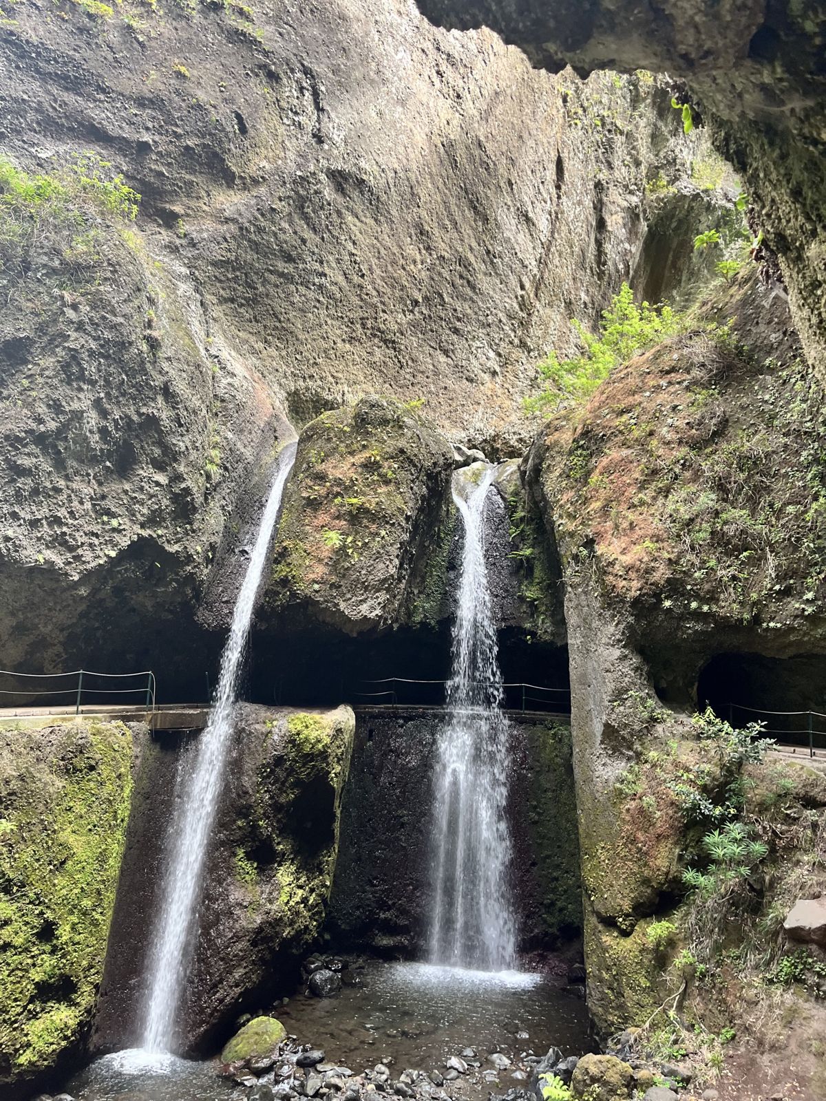 Twin waterfalls under a rock overhang, the levada path passing through a tunnel behind them