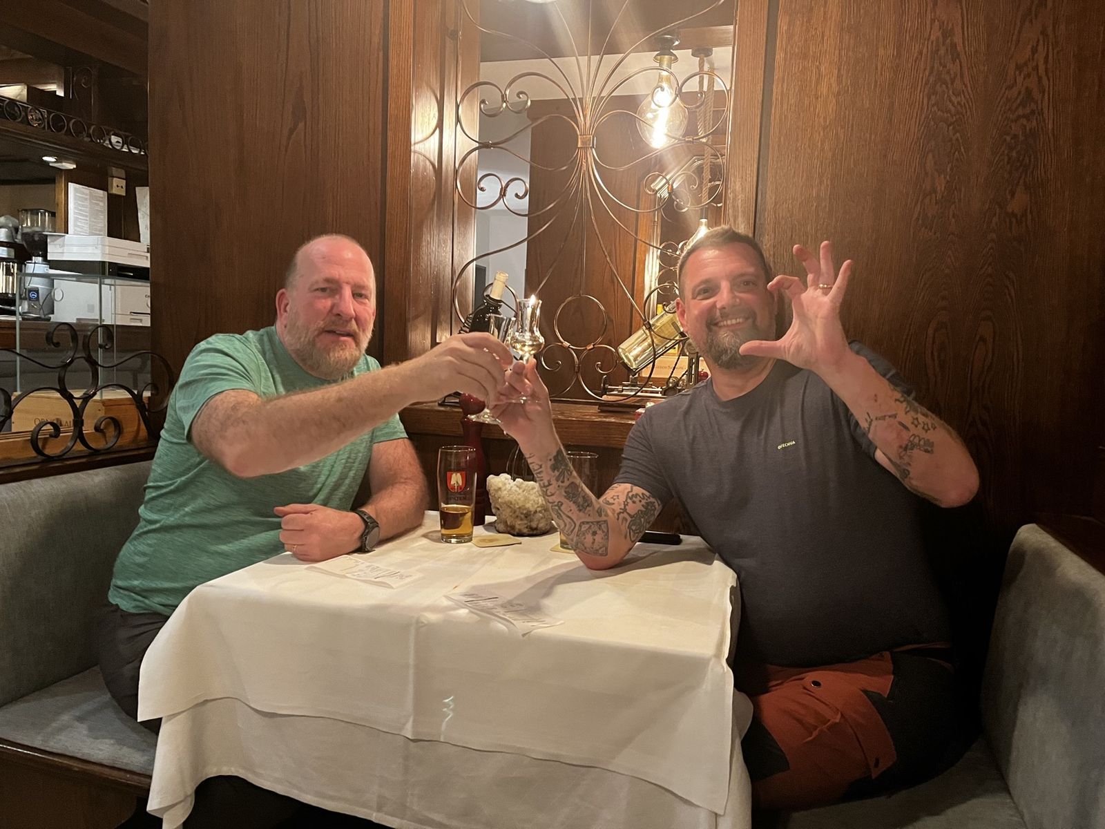 Mike and Nicki clinking small glasses at a white-tablecloth restaurant table