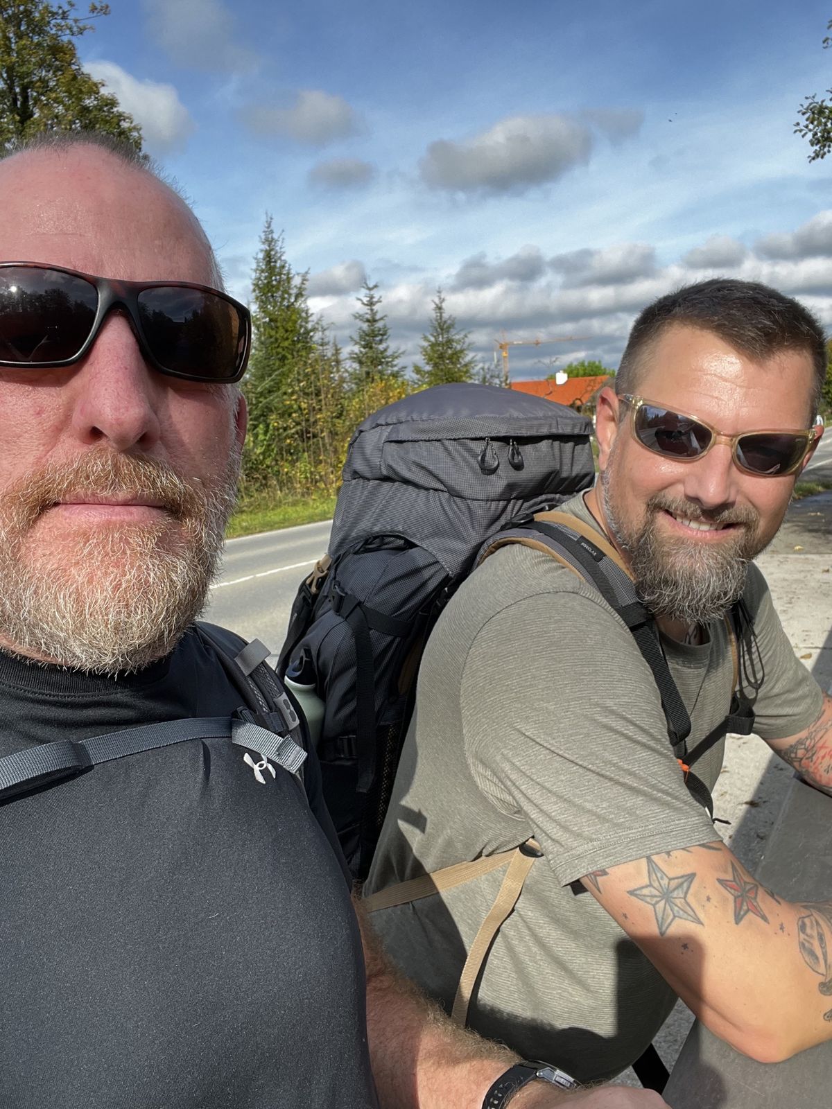 Mike and Nicki resting by a roadside barrier with big packs on a sunny day