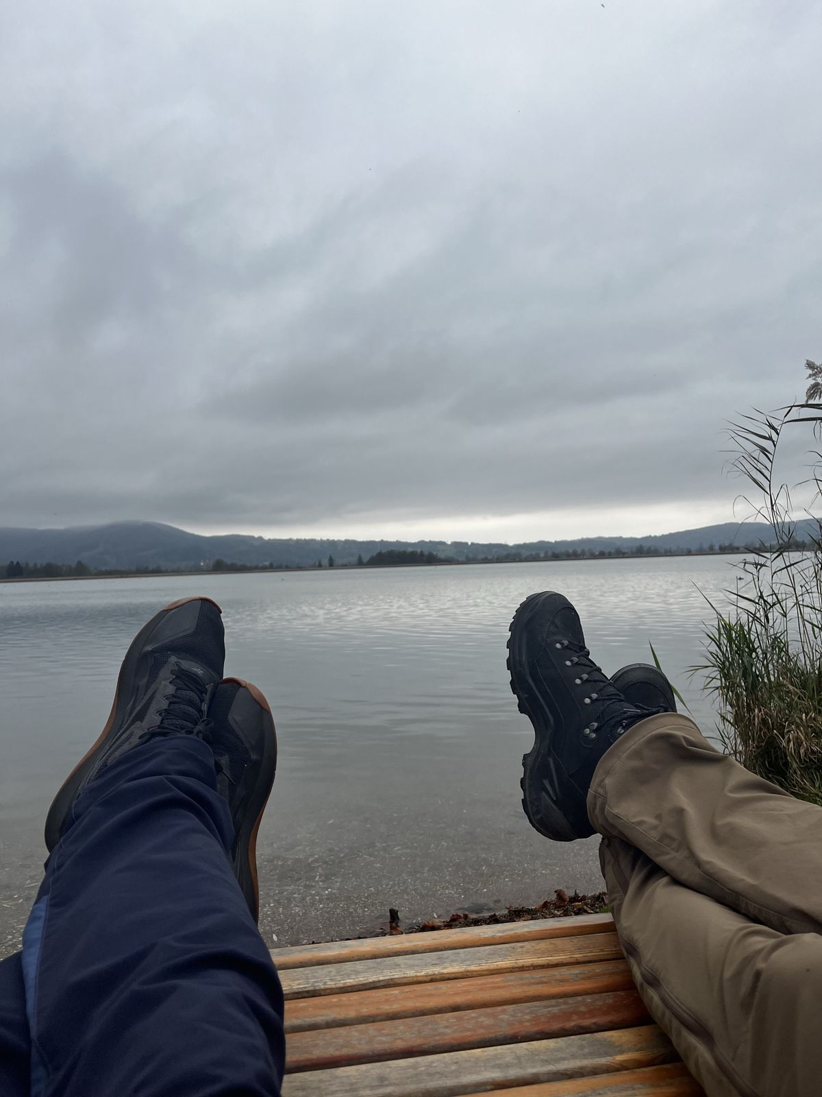 Two pairs of hiking boots resting on a bench overlooking a calm grey lake