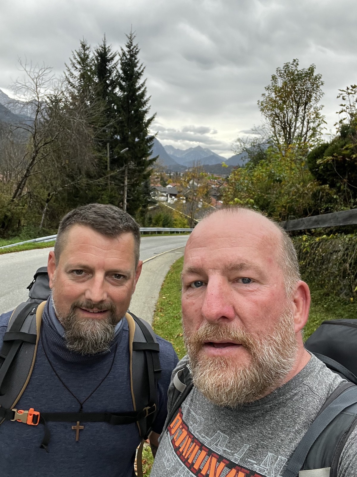Nicki and Mike on a mountain road above a village, the Alps behind under grey skies