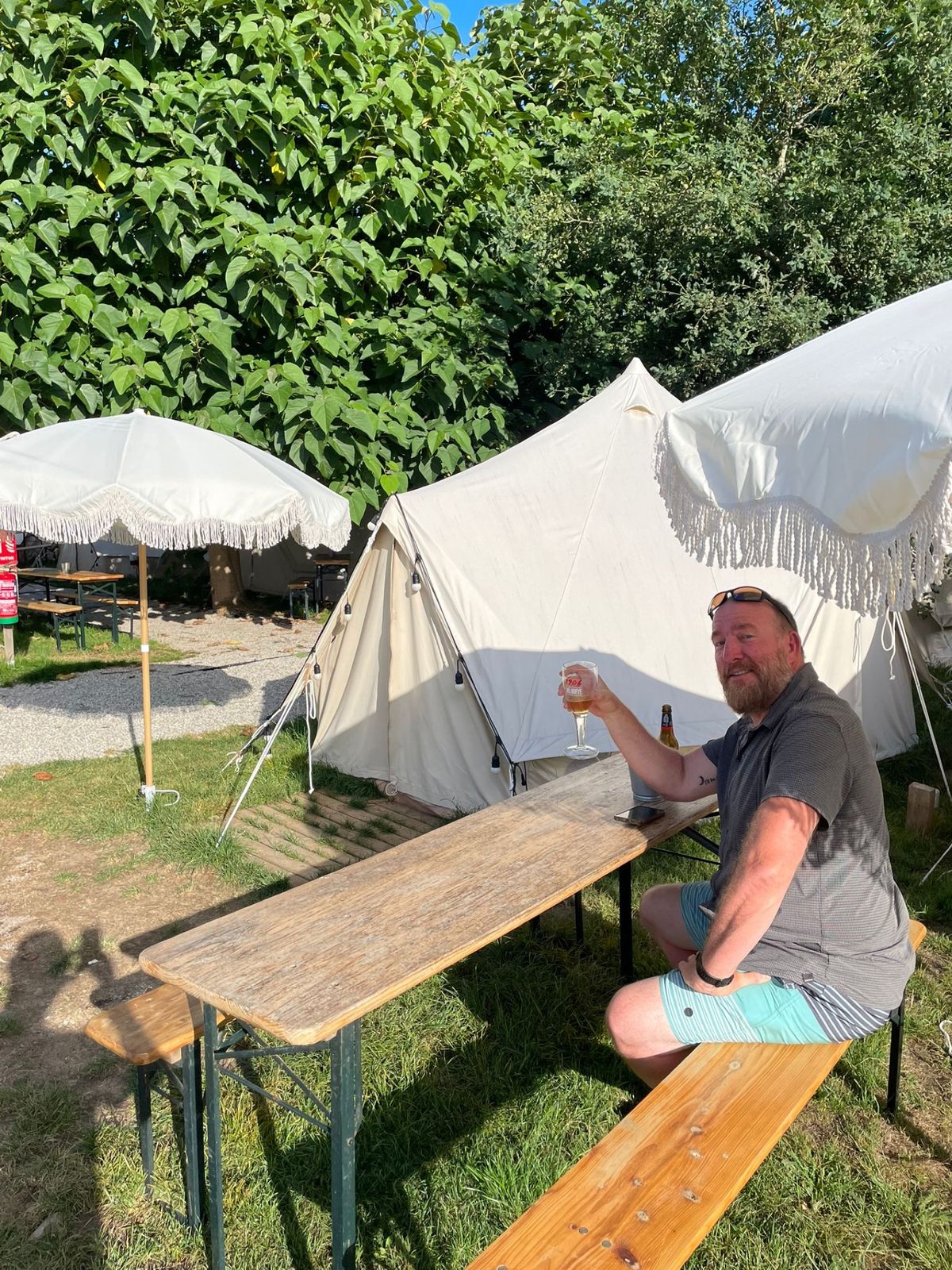 Mike seated at a picnic table in front of a bell tent, raising a glass