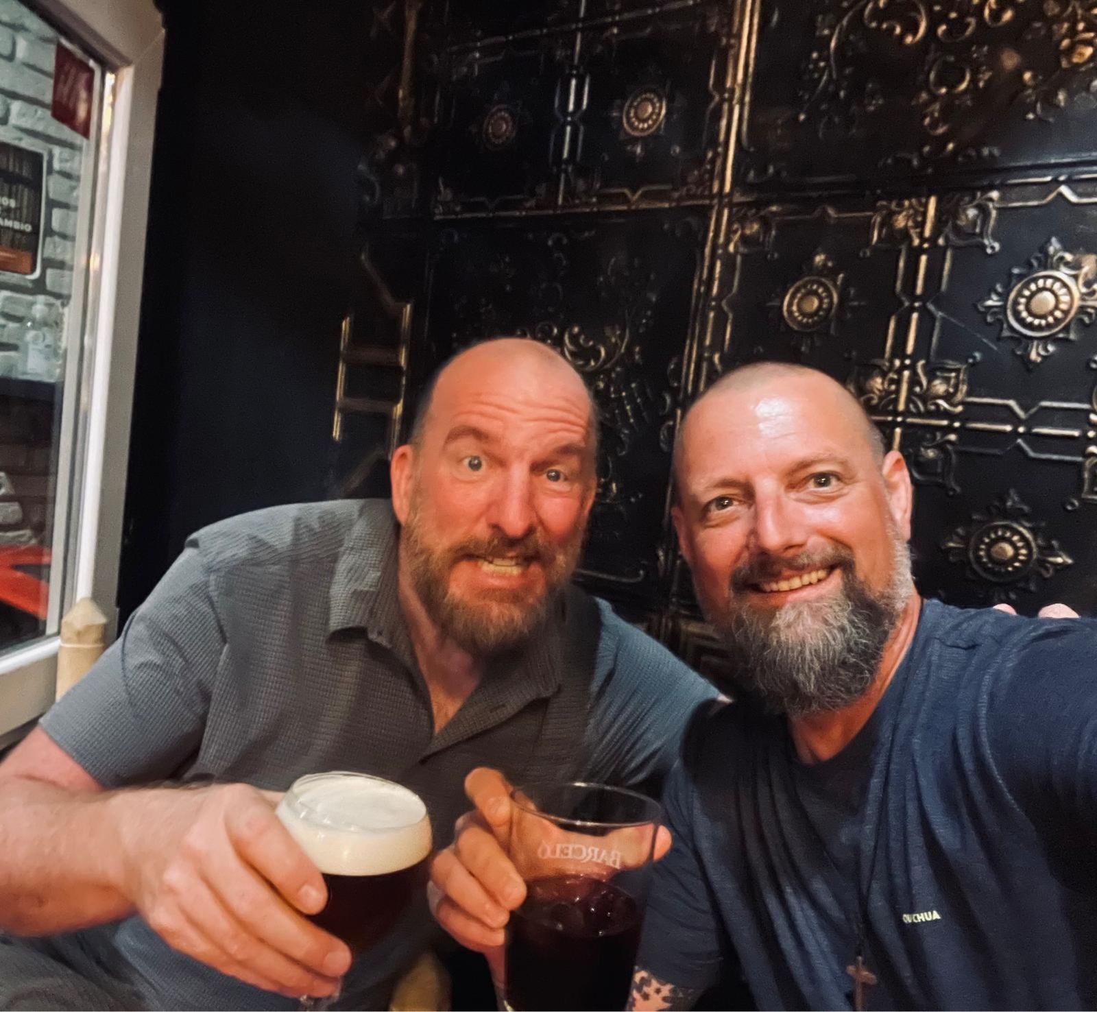 Mike and Nicki holding dark beers in front of an ornate black door