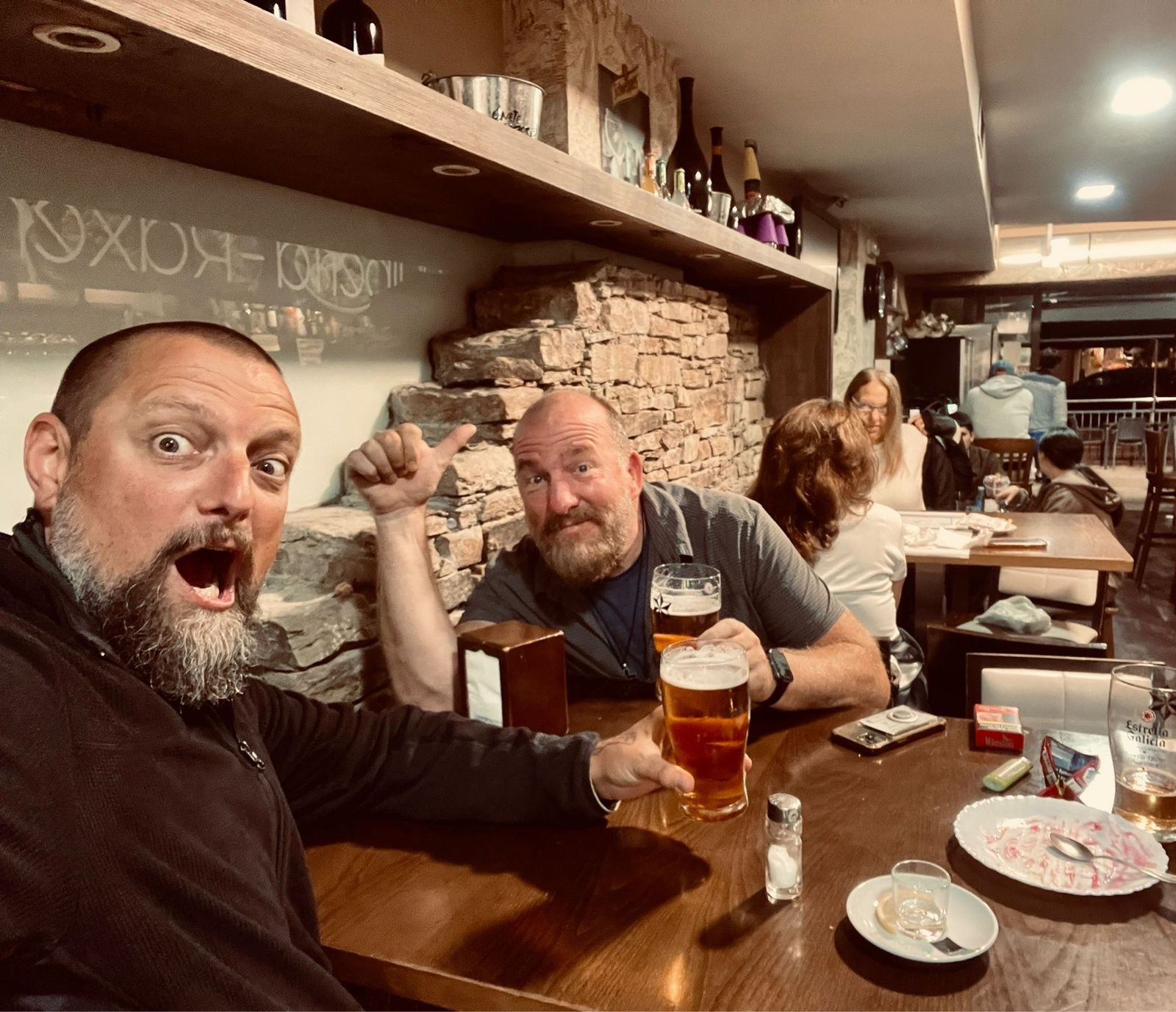 Nicki pulling a face at a restaurant table while Mike gives a thumbs up, beers in hand