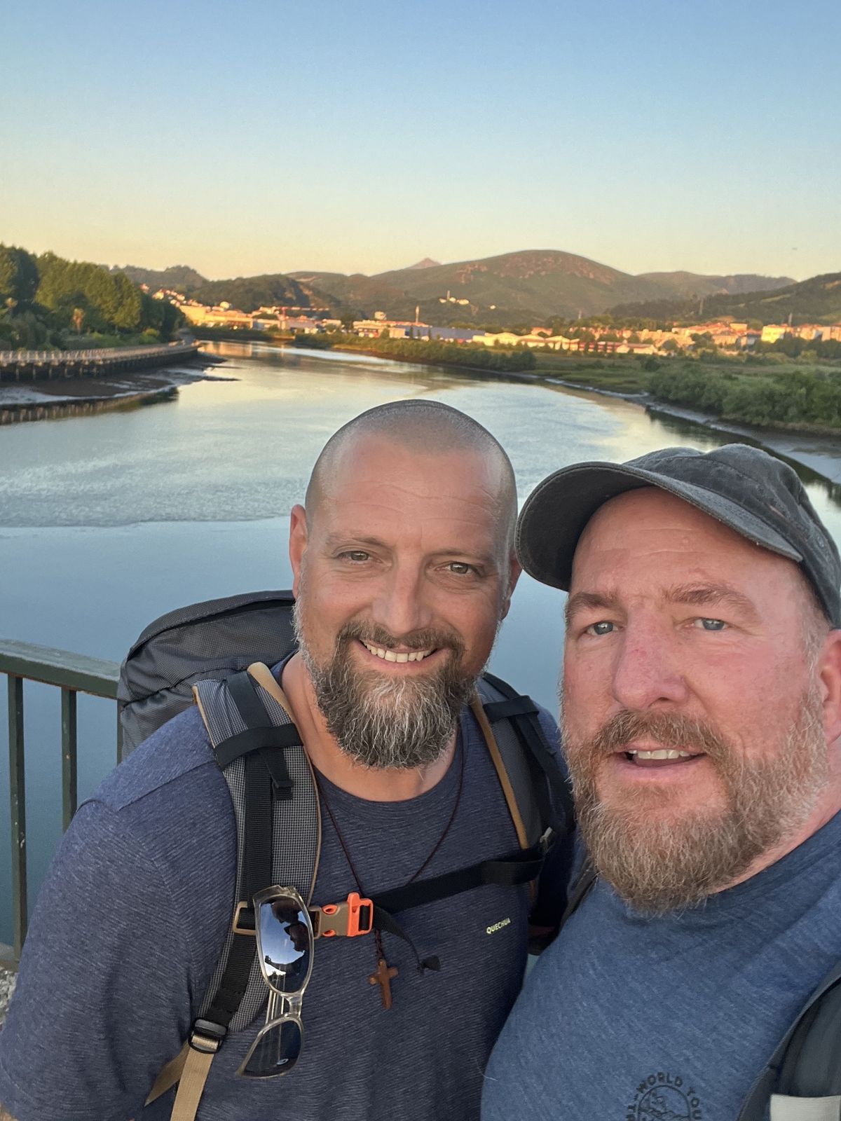 Mike and Nicki selfie on a bridge over a wide river at sunset, hills behind