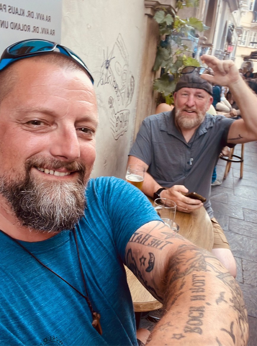 Nicki smiling close to the camera with Mike behind him at a café table