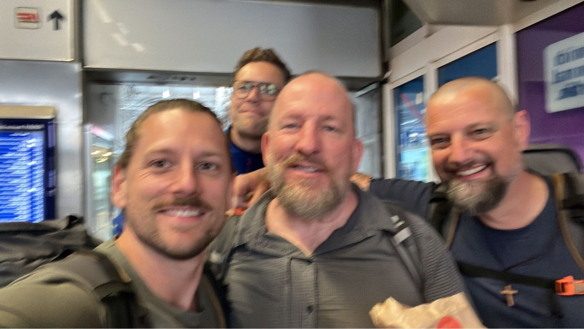 Dennis, Mike and Nicki with a friend at a train station, departure board behind them