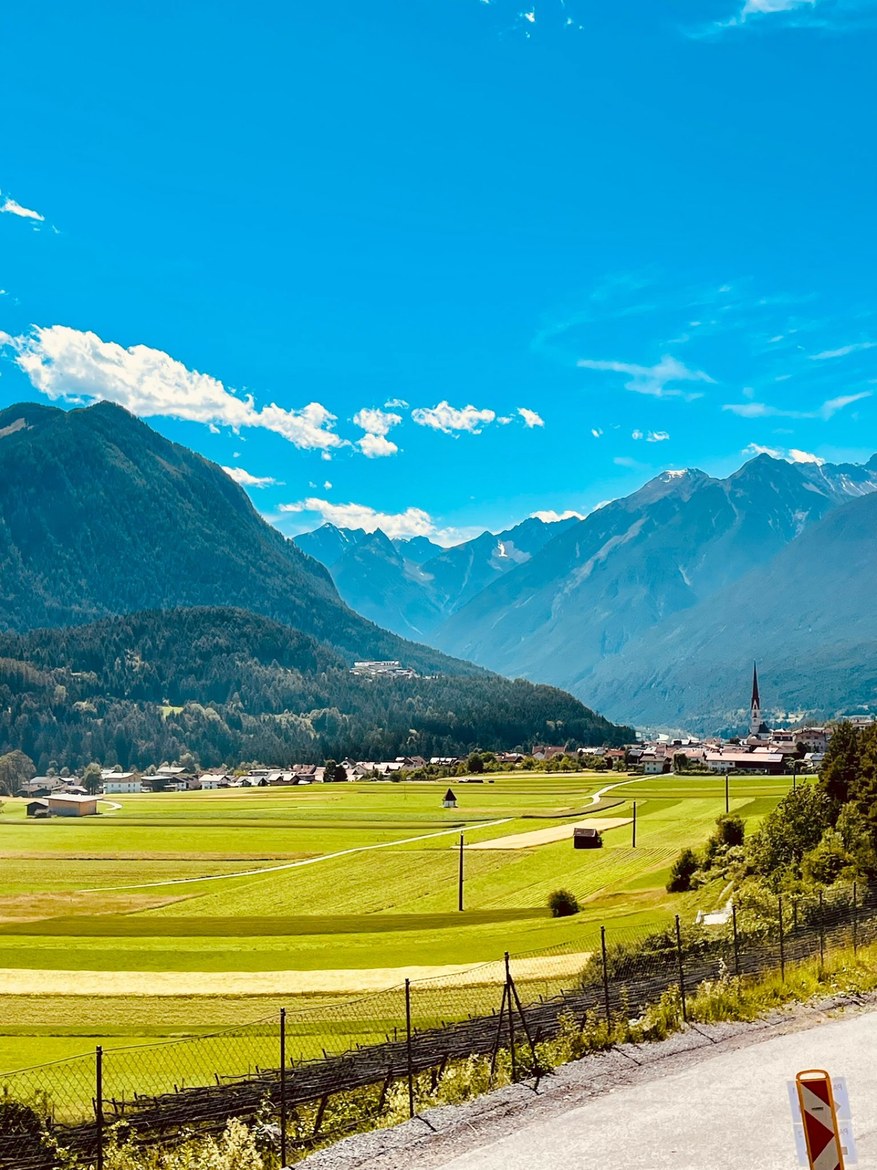 A green alpine valley with a village and church spire below high peaks