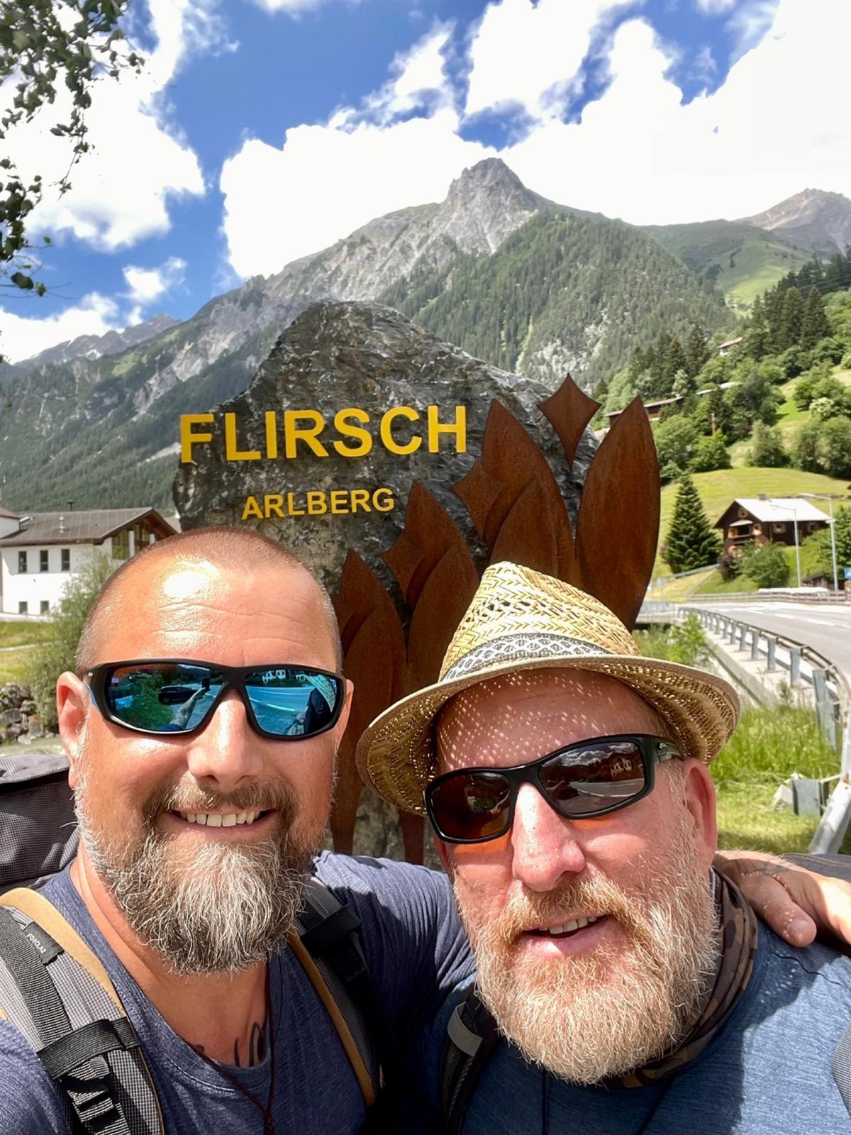 Nicki and Mike taking a selfie at the Flirsch village sign in the Arlberg, peaks behind them