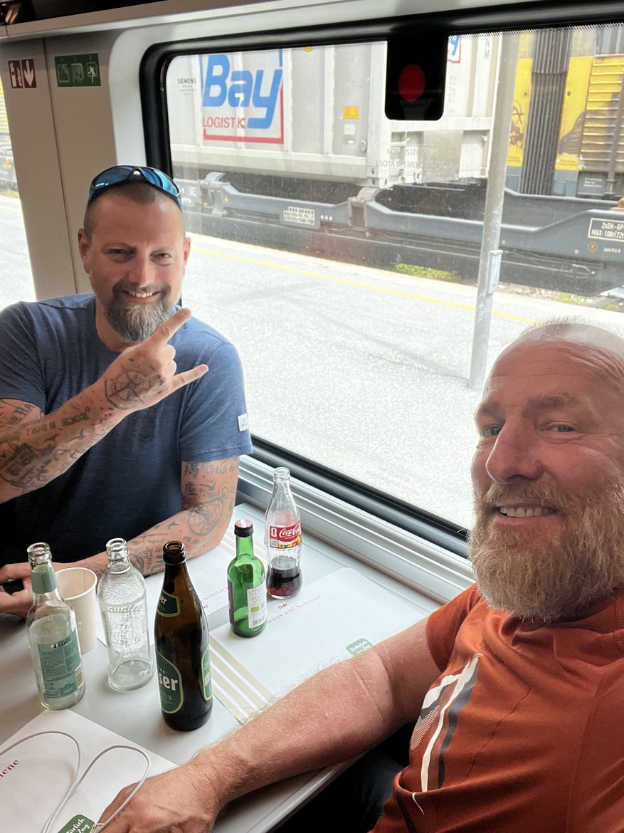Nicki making a hand sign across a train table of empty bottles, Mike beside him
